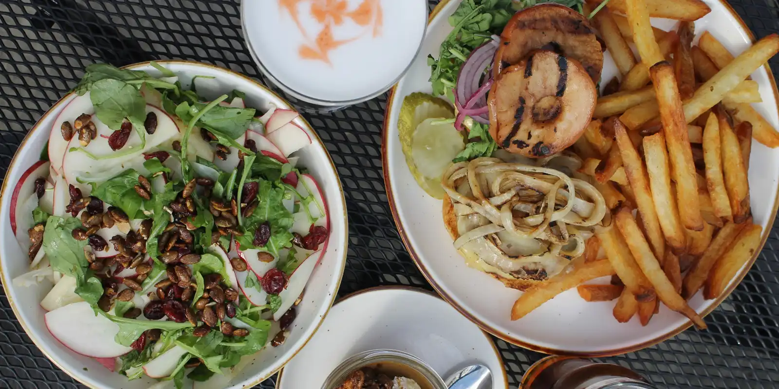 burger, salad, dessert, beer, and a cocktail on a patio table